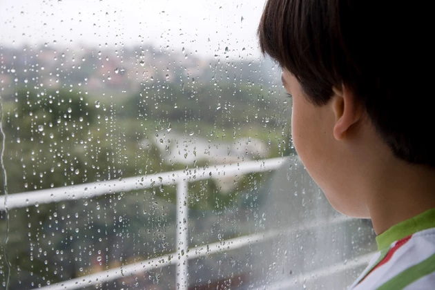 Boy (8-9) looking through window on rainy day
